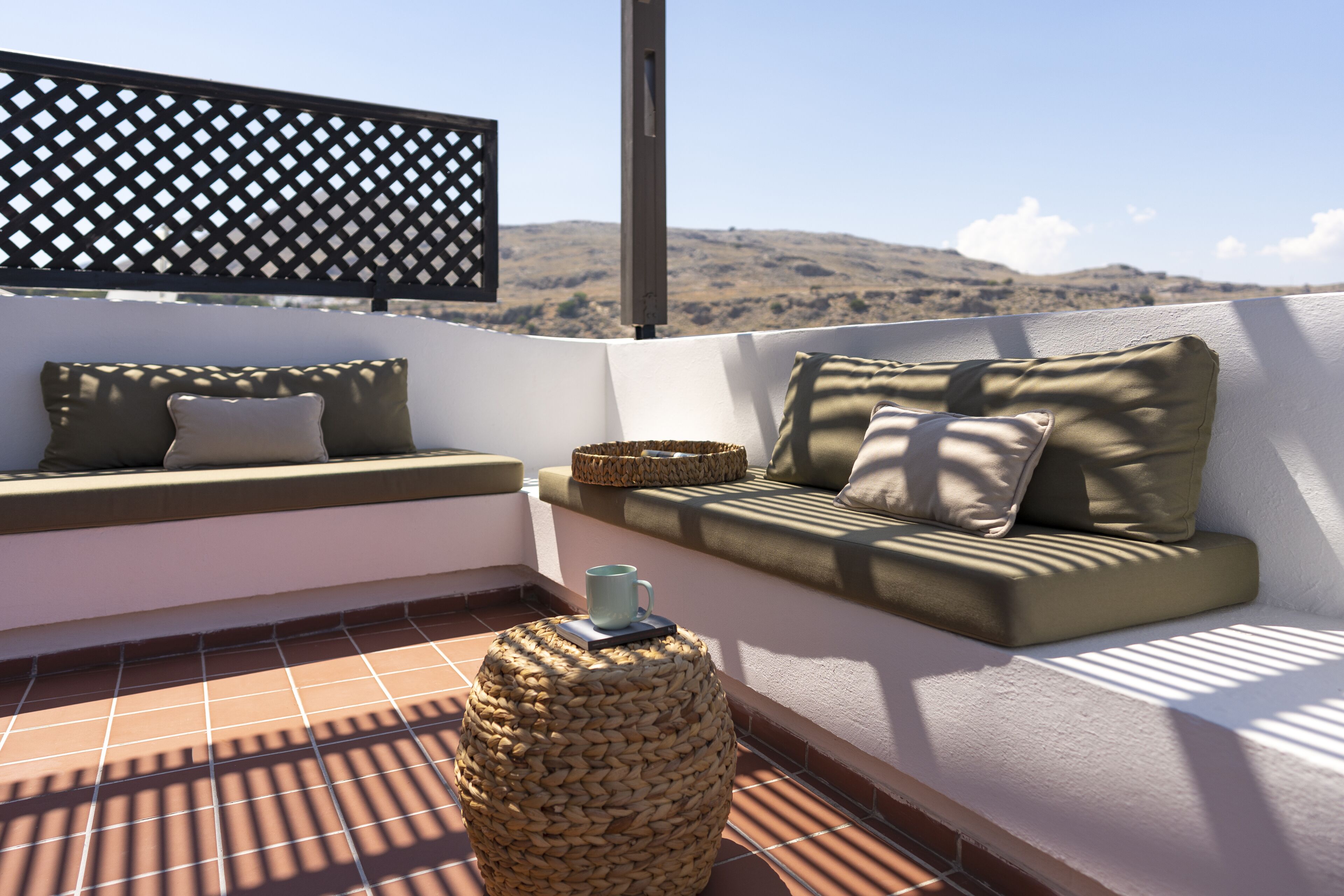 Una terraza en la azotea con zona de estar acolchada, un otoman tejido y vistas a colinas lejanas.