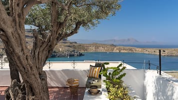 Terraço com uma grande árvore, uma parede branca e vista para o mar.