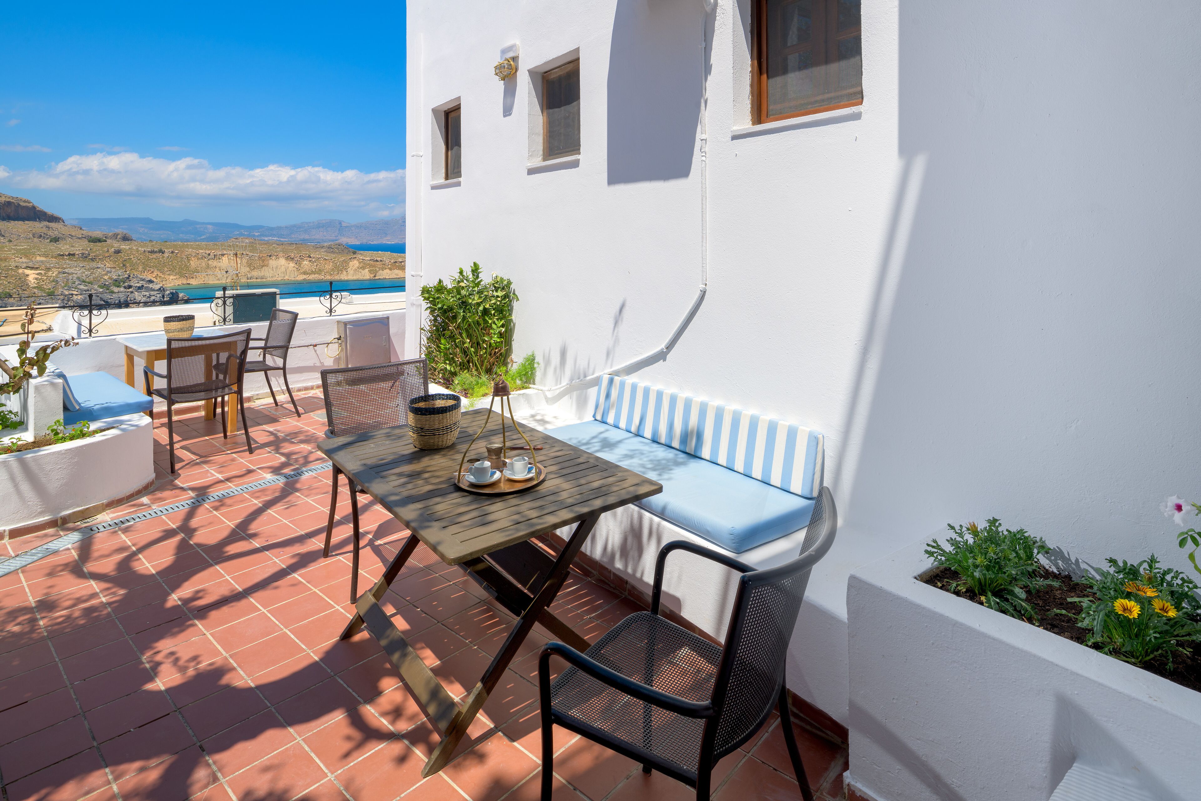 A terrace with a table, chairs, and a bench, overlooking a scenic landscape.