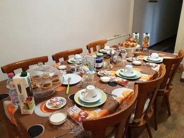A dining table set for breakfast with various food items, plates, and utensils.