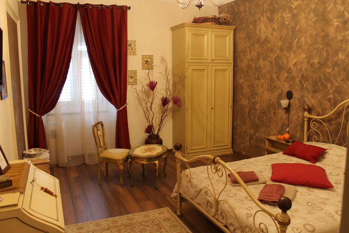 A bedroom with a bed, a wardrobe, a chair, a small table, and a desk.