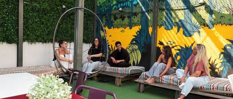 Un grupo de personas sentadas en un banco circular y bancos de madera al aire libre, con un mural de fondo.
