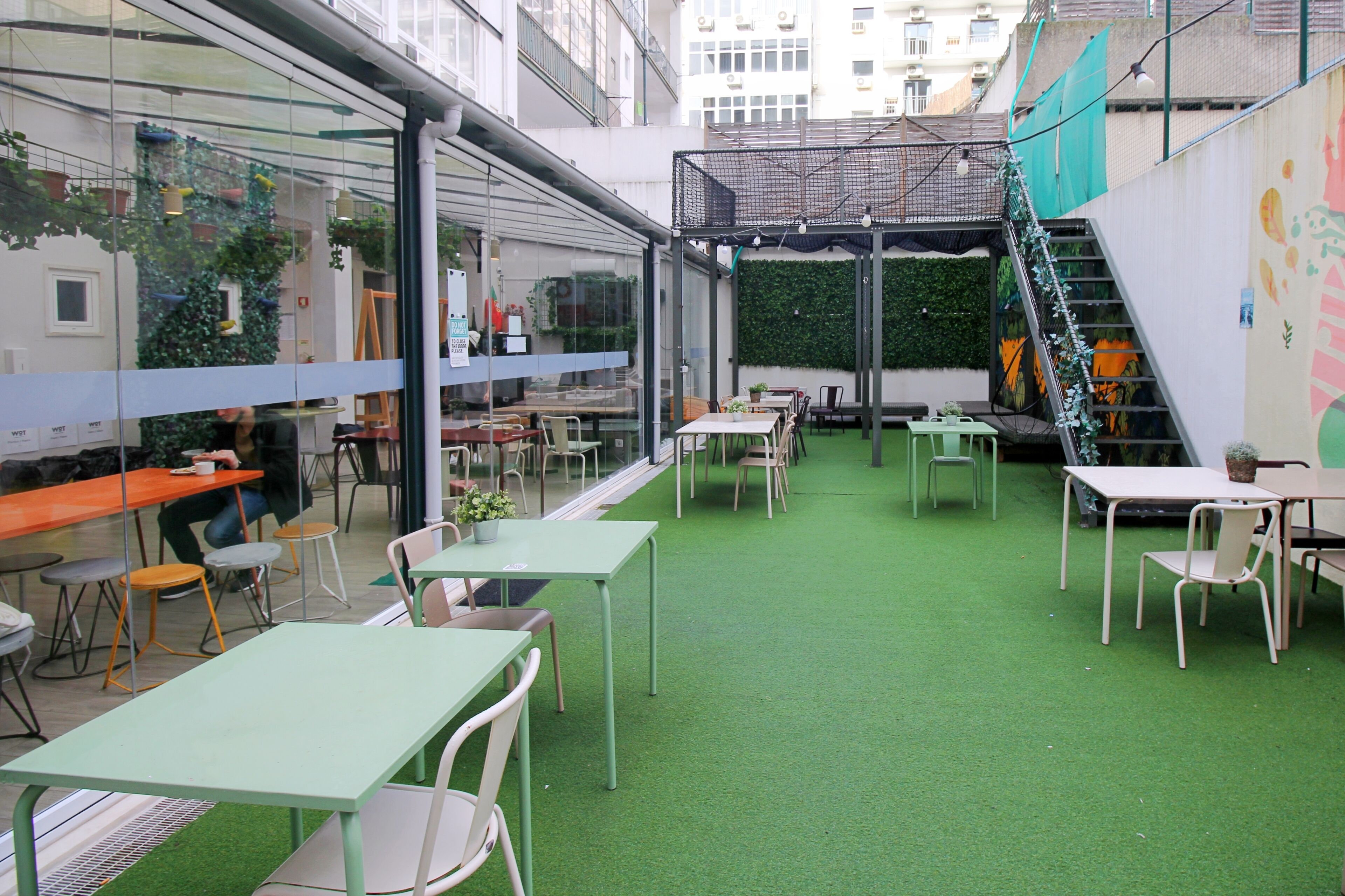An indoor courtyard with tables and chairs, a staircase, and a green wall with plants.