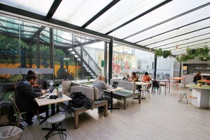 Un café intérieur bénéficiant d’une lumière naturelle, offrant différents types de sièges et une vue sur l’extérieur.