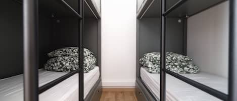 A narrow room with bunk beds, each with patterned pillows.