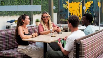 Een groep mensen zit aan een tafel in een terrascafe met uitzicht op groen en een muurschildering op de achtergrond.