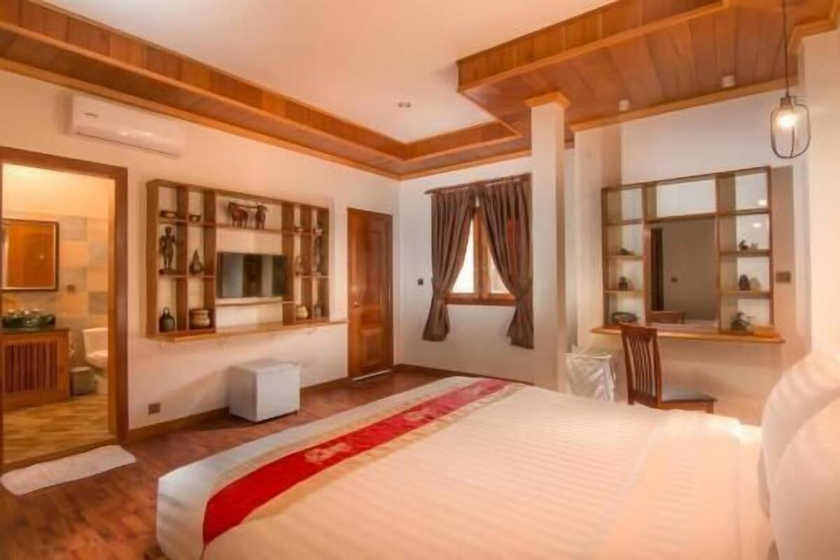 A bedroom with a large bed, a wardrobe, a mirror, and a window with curtains.
