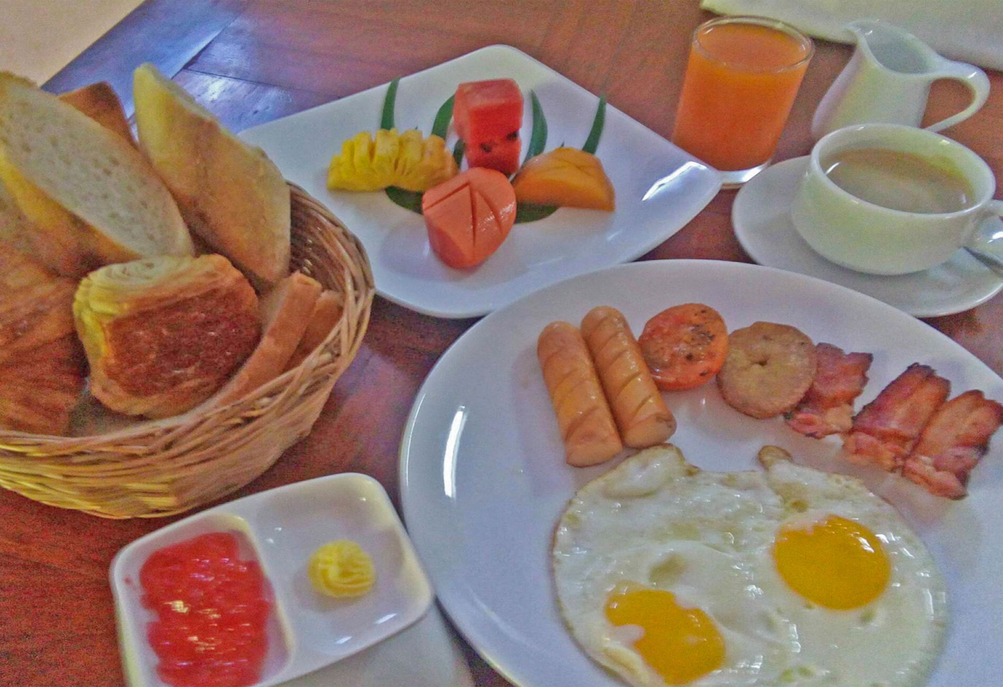 A breakfast table with plates of eggs, sausages, bacon, toast, and fruit.