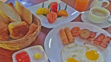 A breakfast table with plates of eggs, sausages, bacon, toast, and fruit.