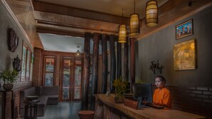 A reception area with a wooden desk, a computer, and a potted plant. There are stools and a bench in the background. - BB Angkor Residence (Siem Reap)
