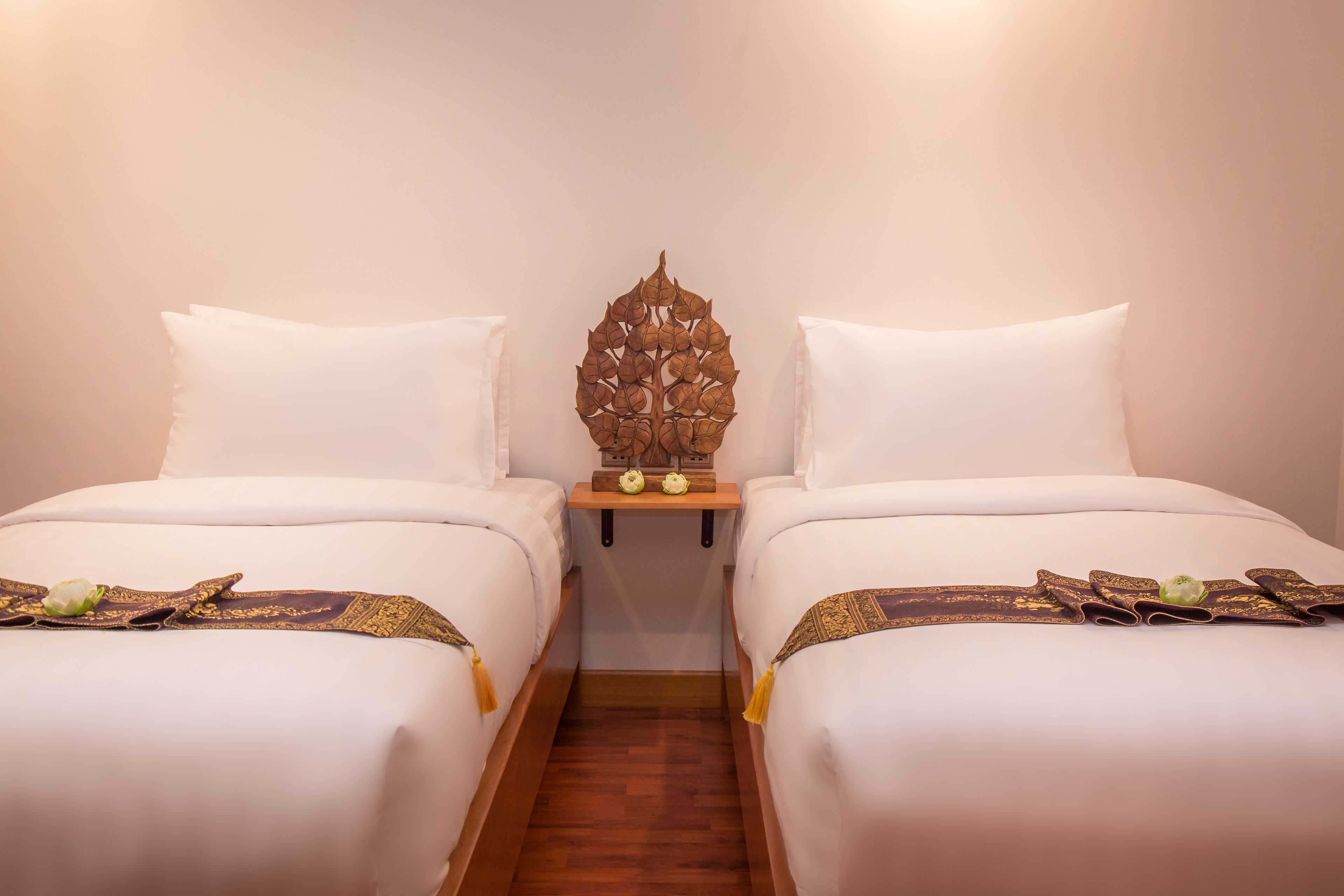 A hotel room with two single beds, a wooden nightstand with a decorative item, and a small table with a green flower.