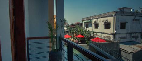 A balcony with a potted plant, a patterned floor, and red umbrellas in the background.