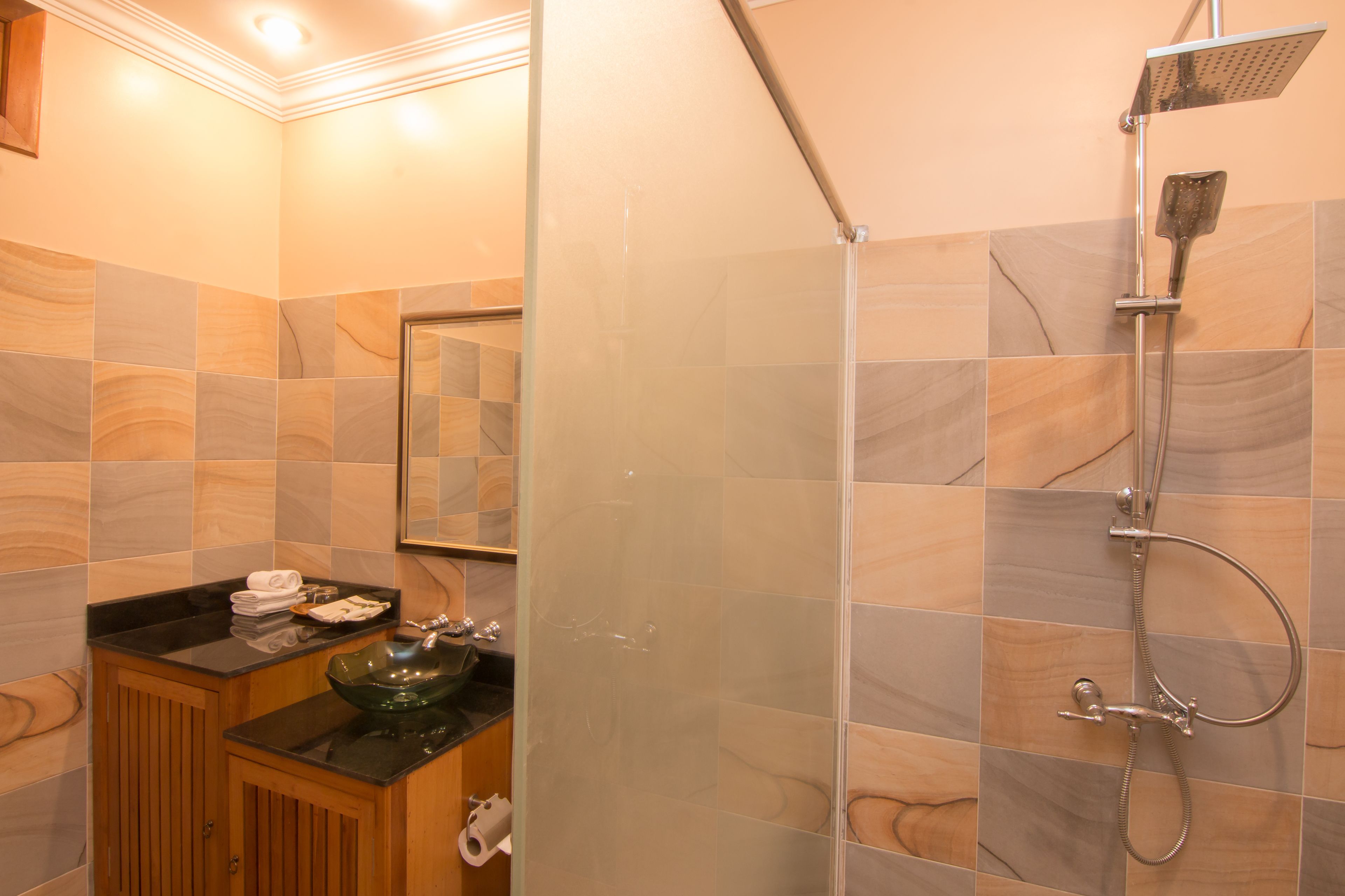 A modern bathroom with a glass-enclosed shower, a wooden vanity, and a glass sink.