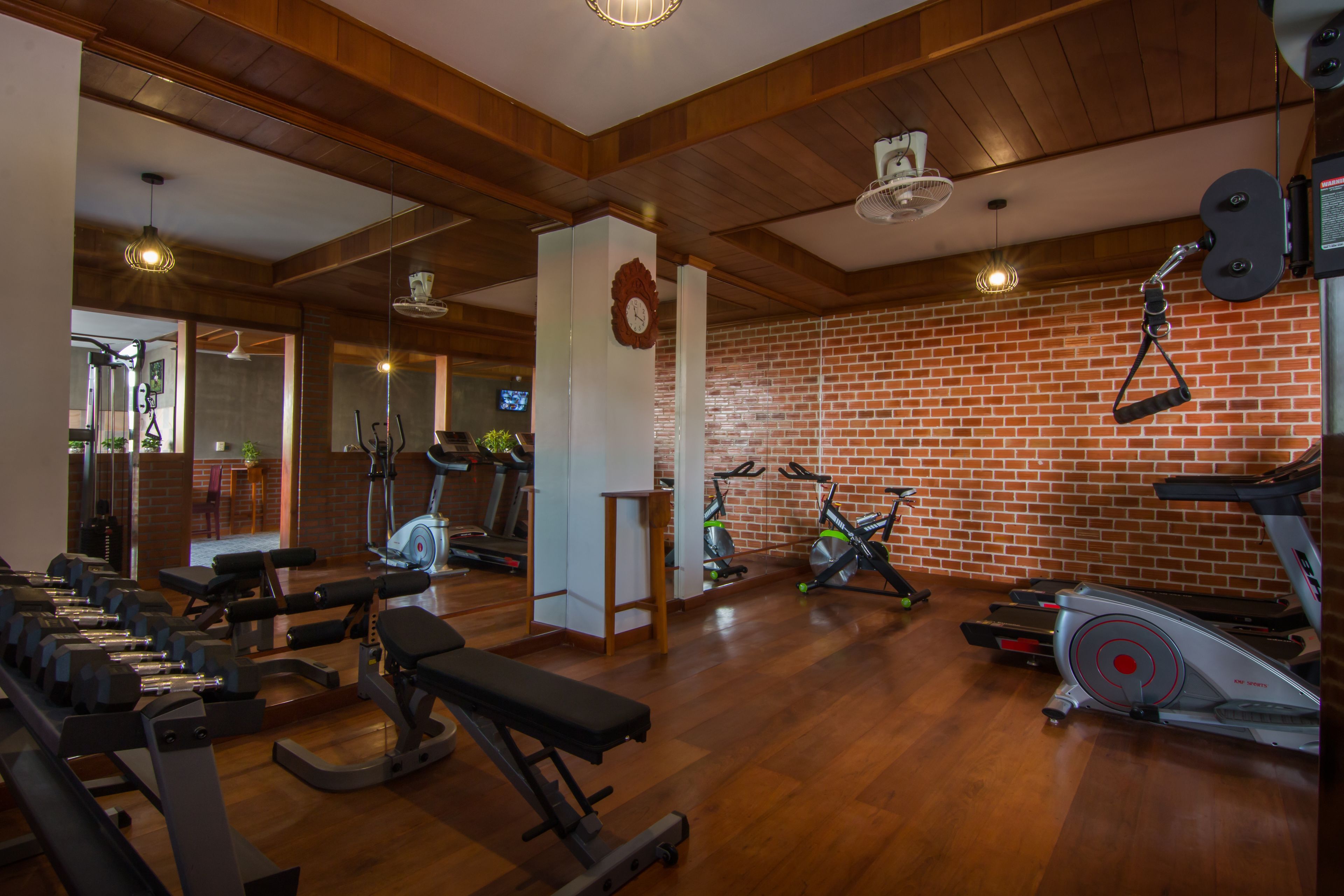 Een sportschool met diverse fitnessapparaten, houten vloeren en bakstenen muren.