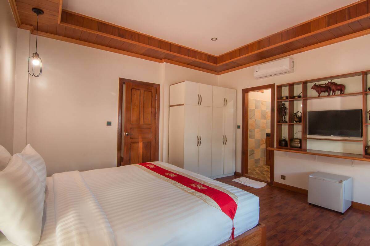 A bedroom with a bed, wardrobe, TV, and a small refrigerator.