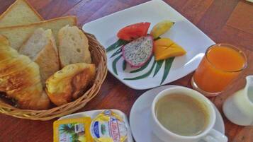 Une table dressée pour le petit-déjeuner avec des toasts, des viennoiseries, une assiette de fruits, une tasse de café et un verre de jus d’orange.