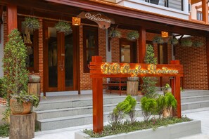 A wooden sign with "Welcome" above a restaurant entrance, surrounded by potted plants and steps leading up to the door. - BB Angkor Residence (Siem Reap)
