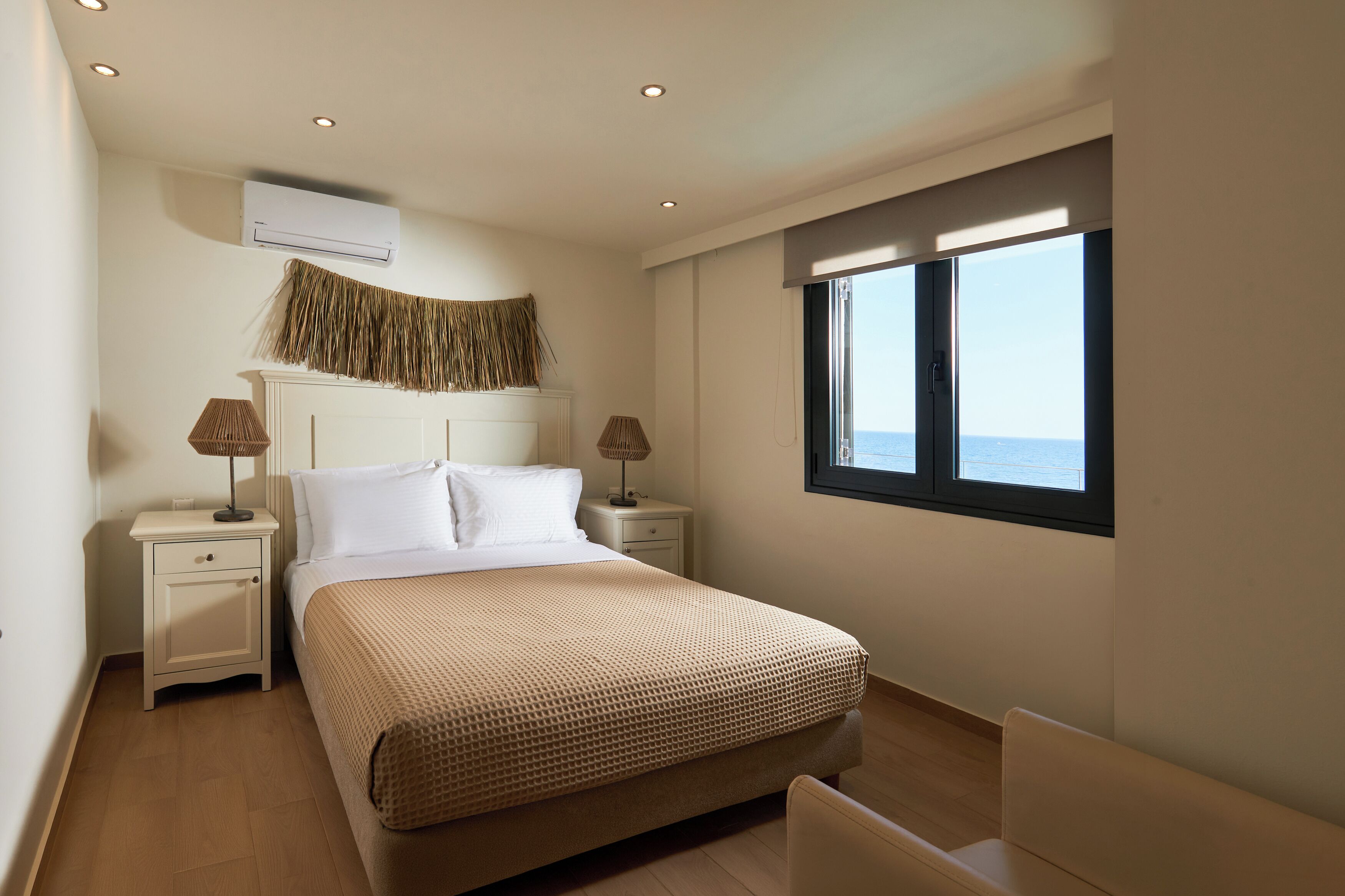 Un dormitorio con cama, mesitas de noche, lámparas, aire acondicionado, ventana con vistas e iluminación empotrada en el techo.