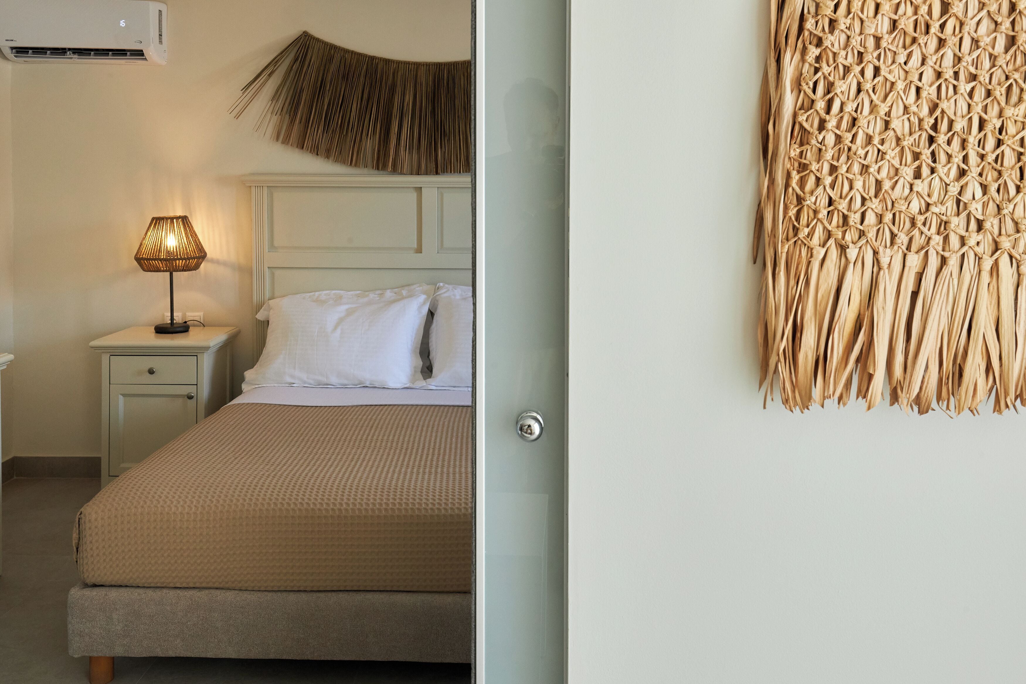 A bedroom with a bed, nightstand, lamp, and a woven wall hanging.