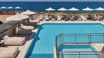 Zona de piscina con sillas de descanso y sombrillas, vista despejada al mar y piscina con azulejos.