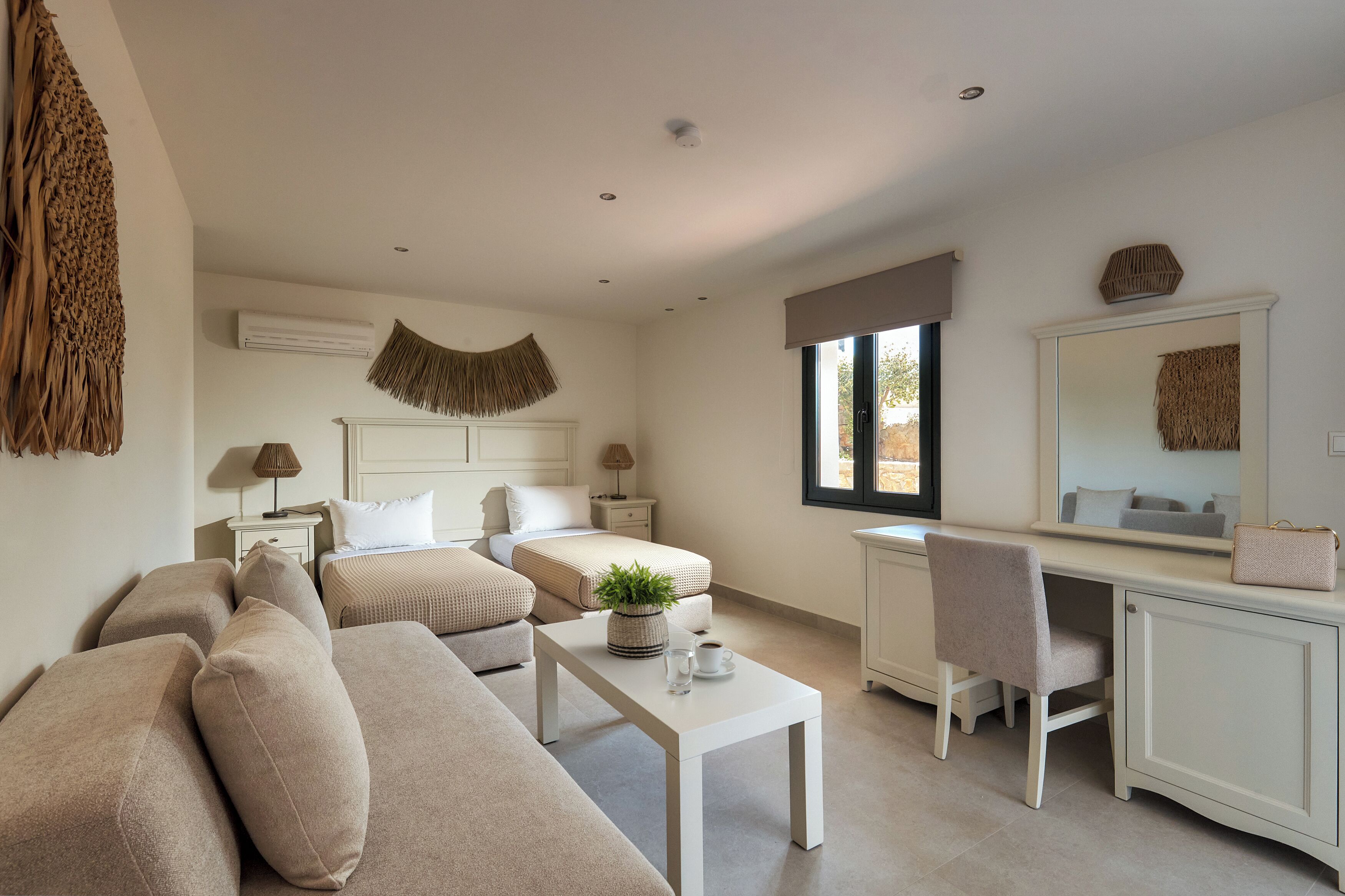 A bedroom with two beds, a desk, a chair, a bedside table, and a large mirror.