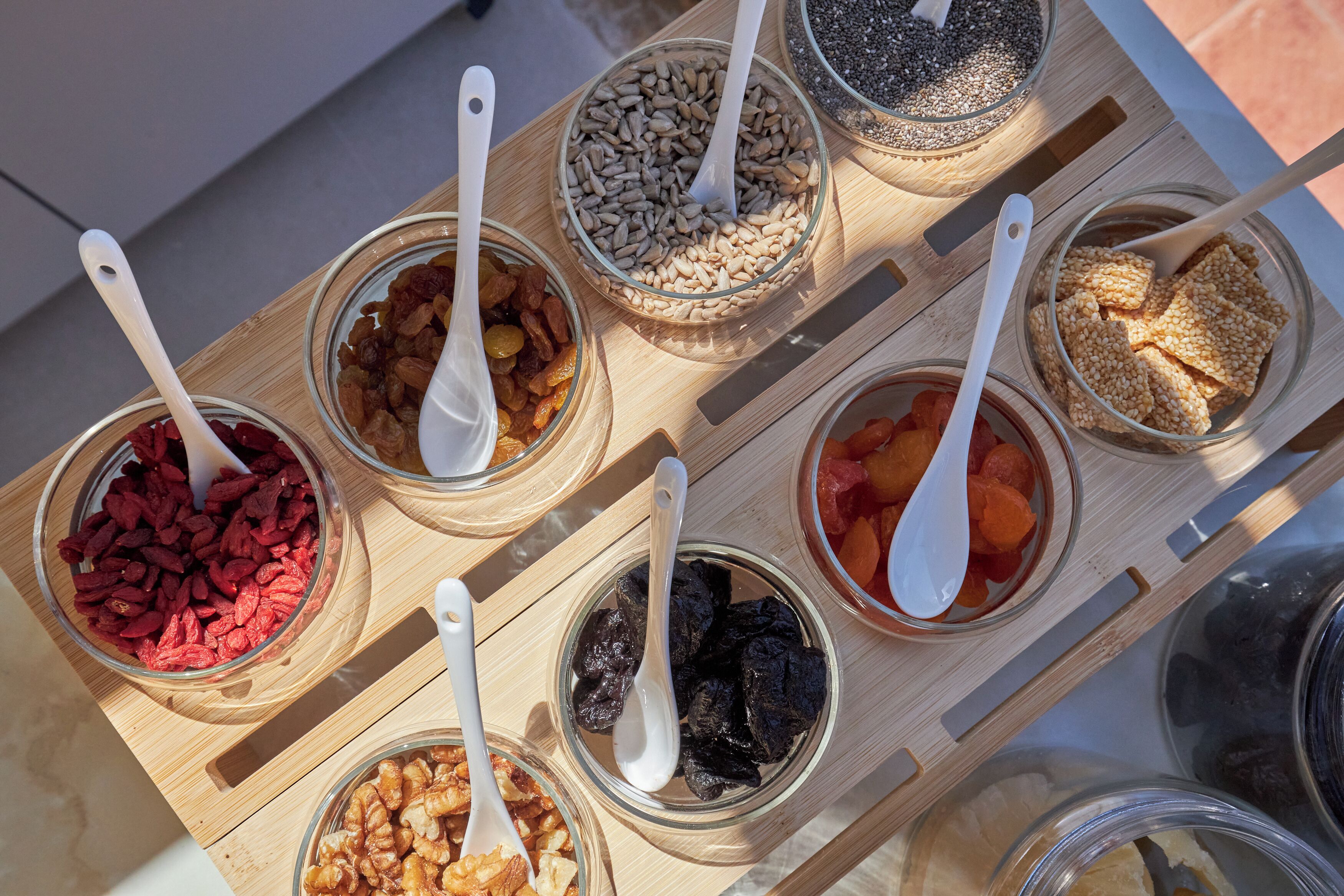 Una bandeja de madera con recipientes de vidrio que contienen diversas frutas secas y nueces.