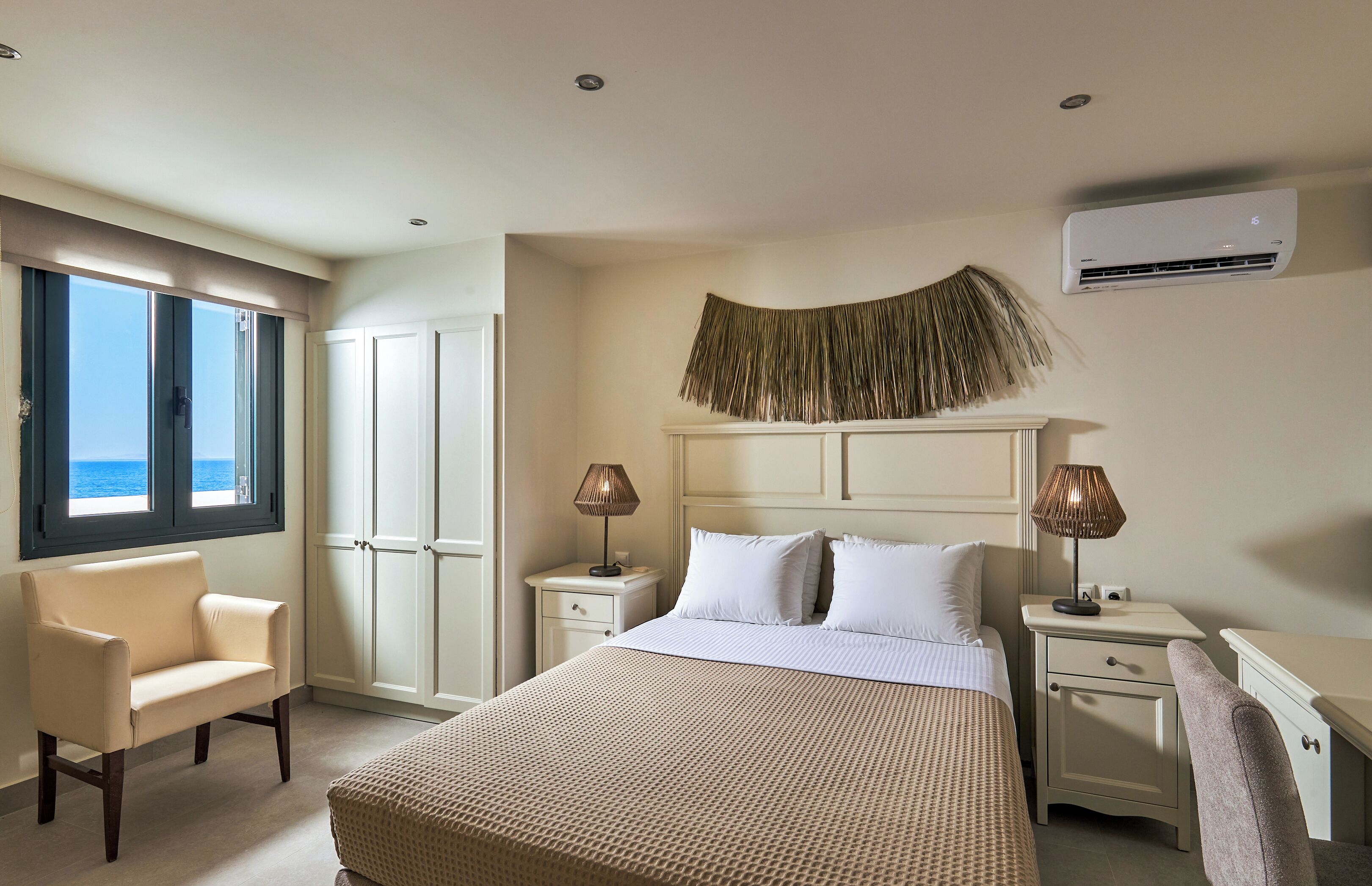 A hotel room with a bed, bedside tables, a chair, a wardrobe, and a view of the sea.