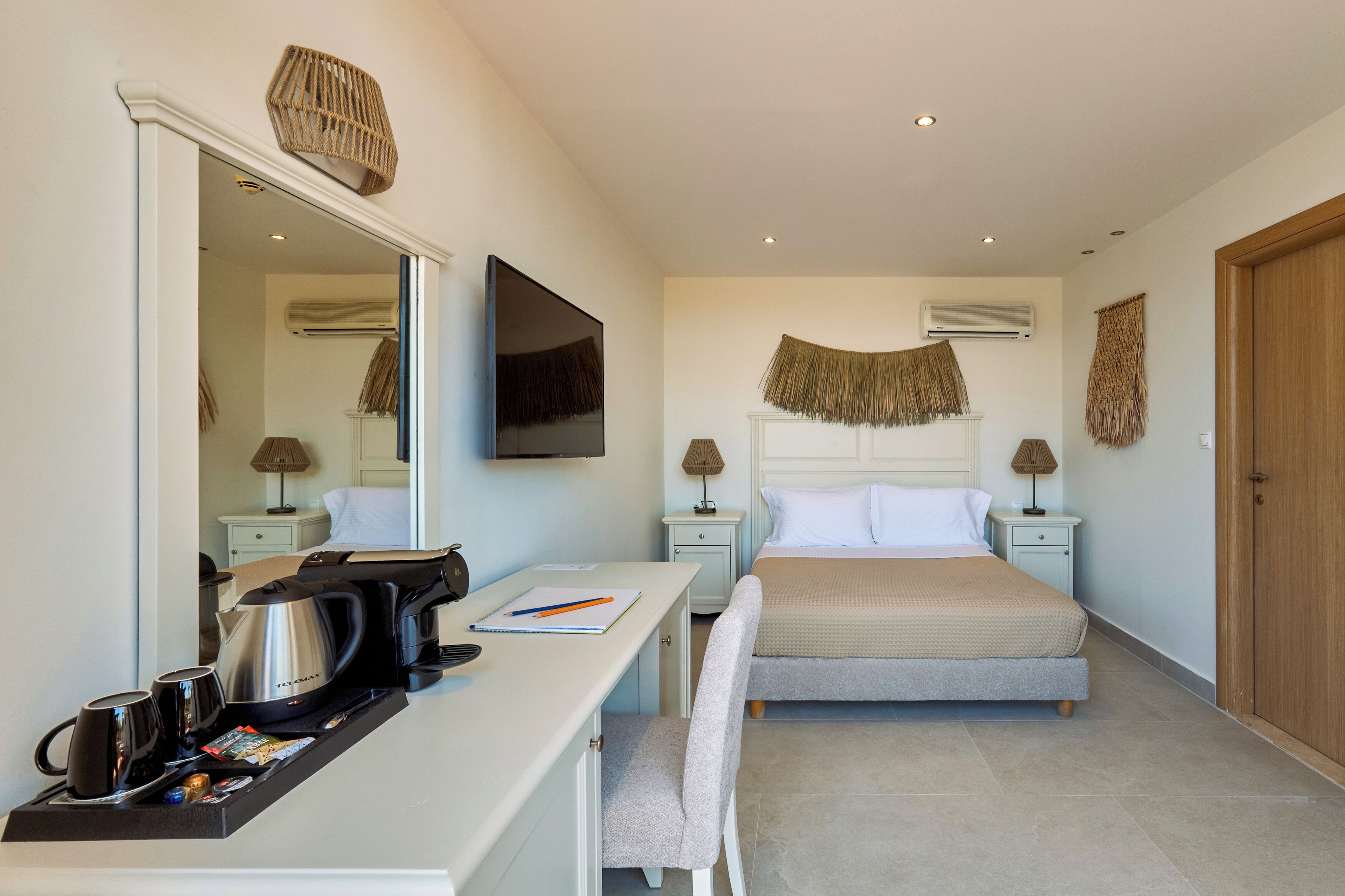 Une chambre d’hôtel moderne équipée d’un lit, d’un bureau avec une bouilloire, d’une télévision à écran plat et d’un grand miroir.