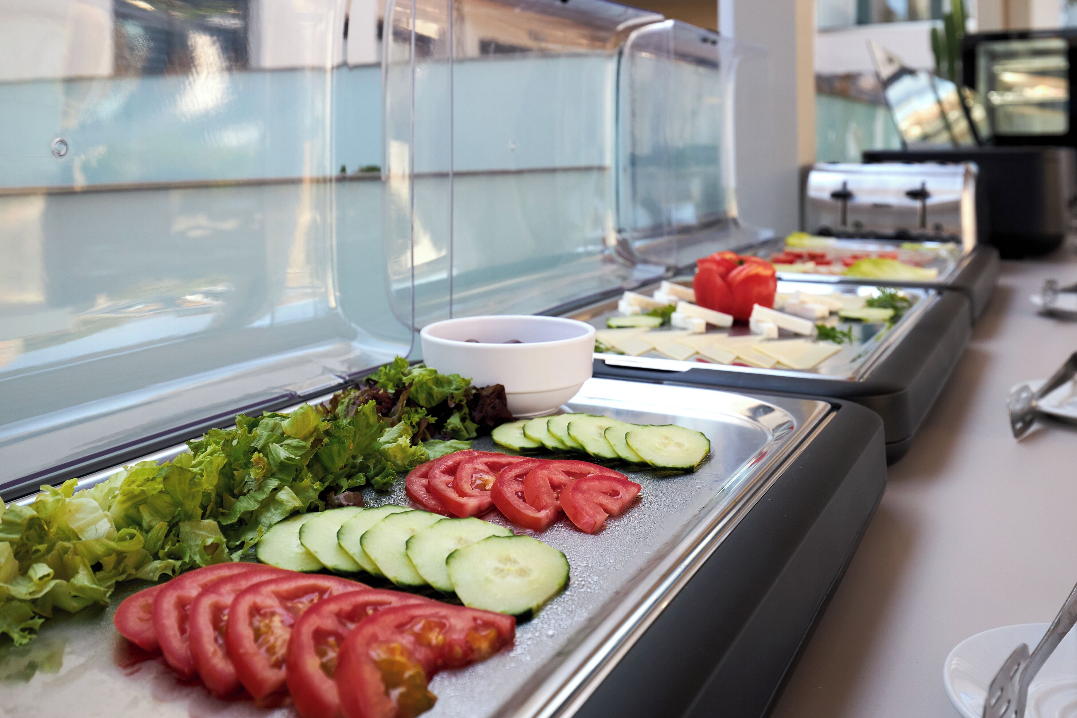 A buffet with various food items including sliced cucumbers, tomatoes, and lettuce.