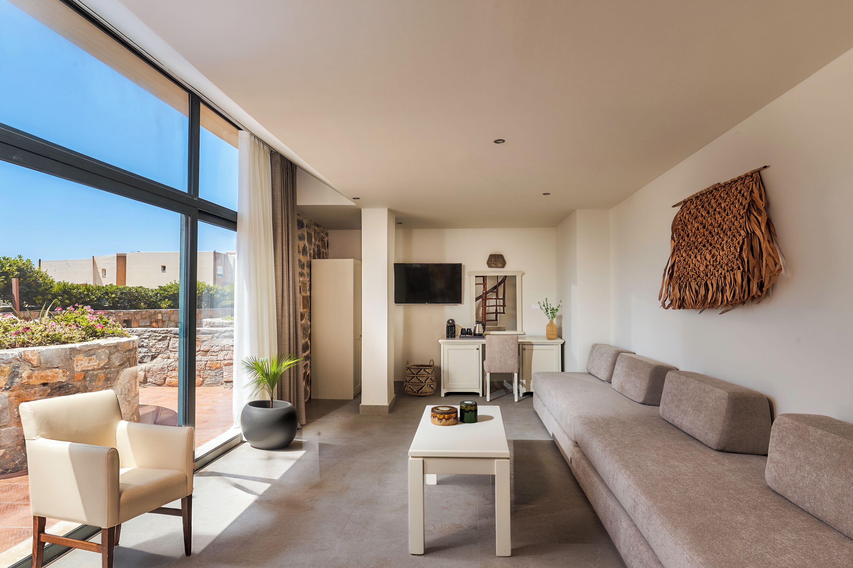 Un salon moderne avec un canapé, un fauteuil, une table basse, un téléviseur et une grande fenêtre.