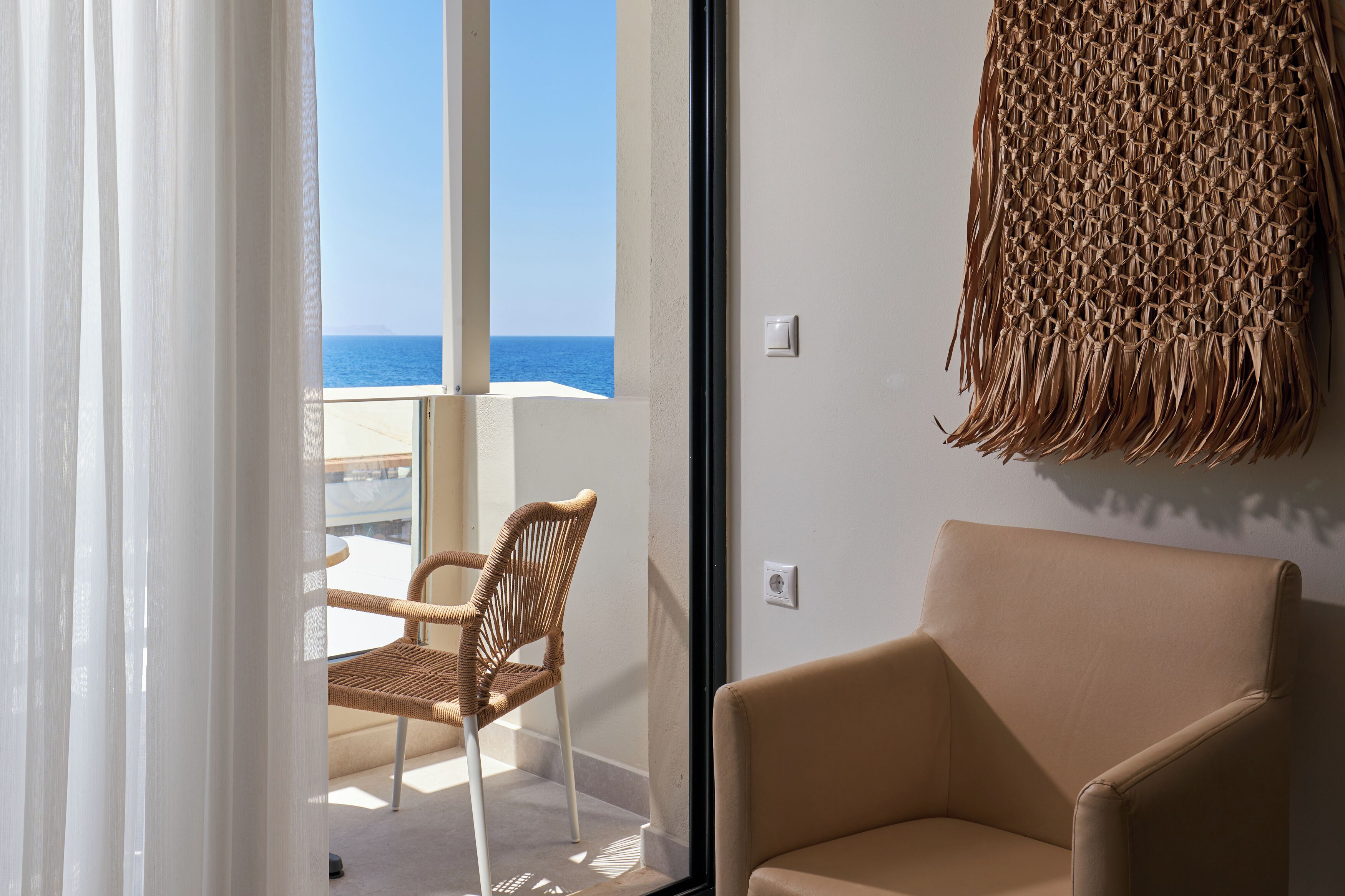 Una habitación con vista al mar, una silla de mimbre, un sofá y un tapiz de pared tejido.