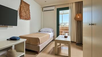 A hotel room with a bed, a desk, a TV, an air conditioner, a window with curtains, and a view of the outside.