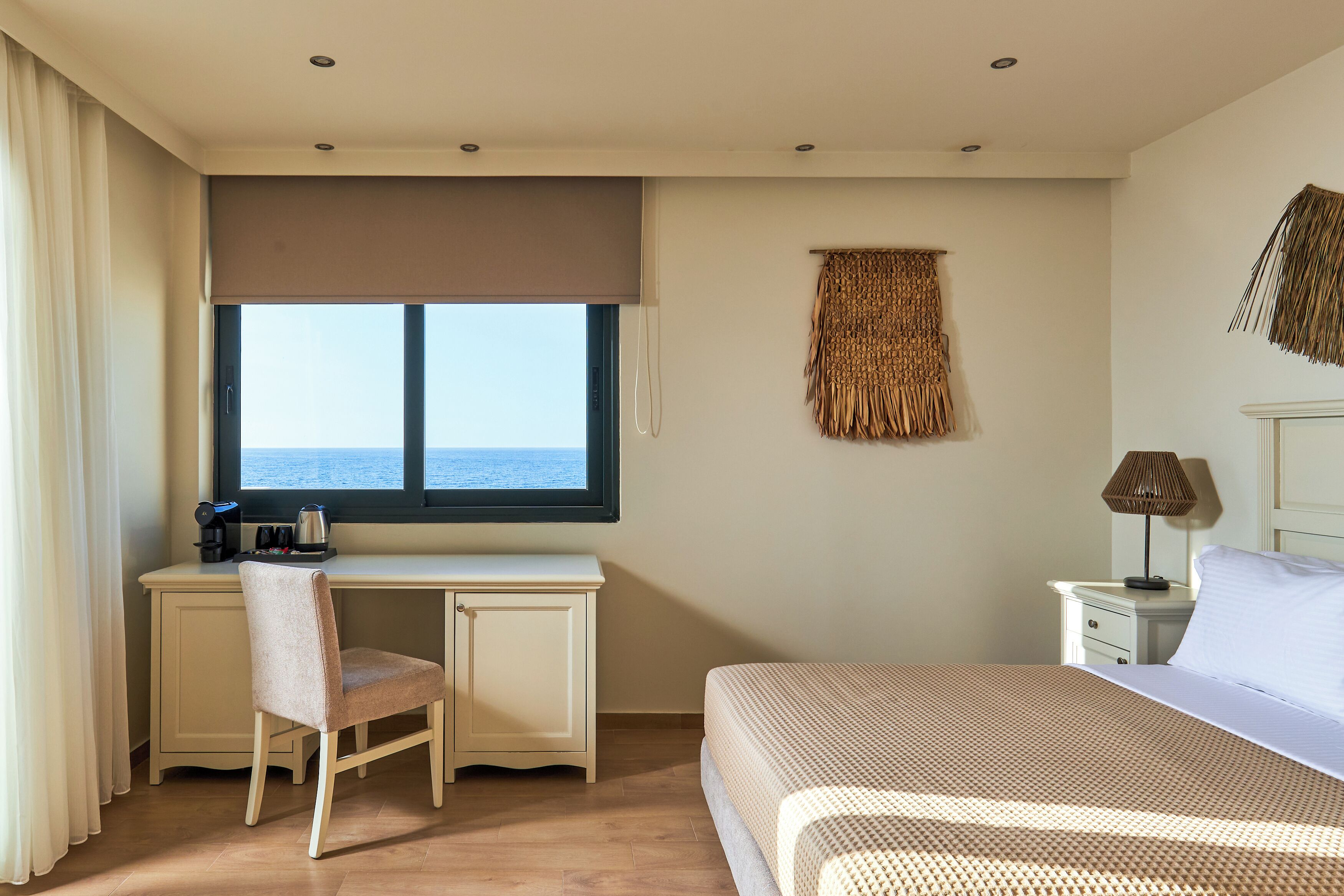 Un dormitorio con cama, escritorio, silla, mesita de noche, lámpara, ventana con vistas y un adorno en la pared.