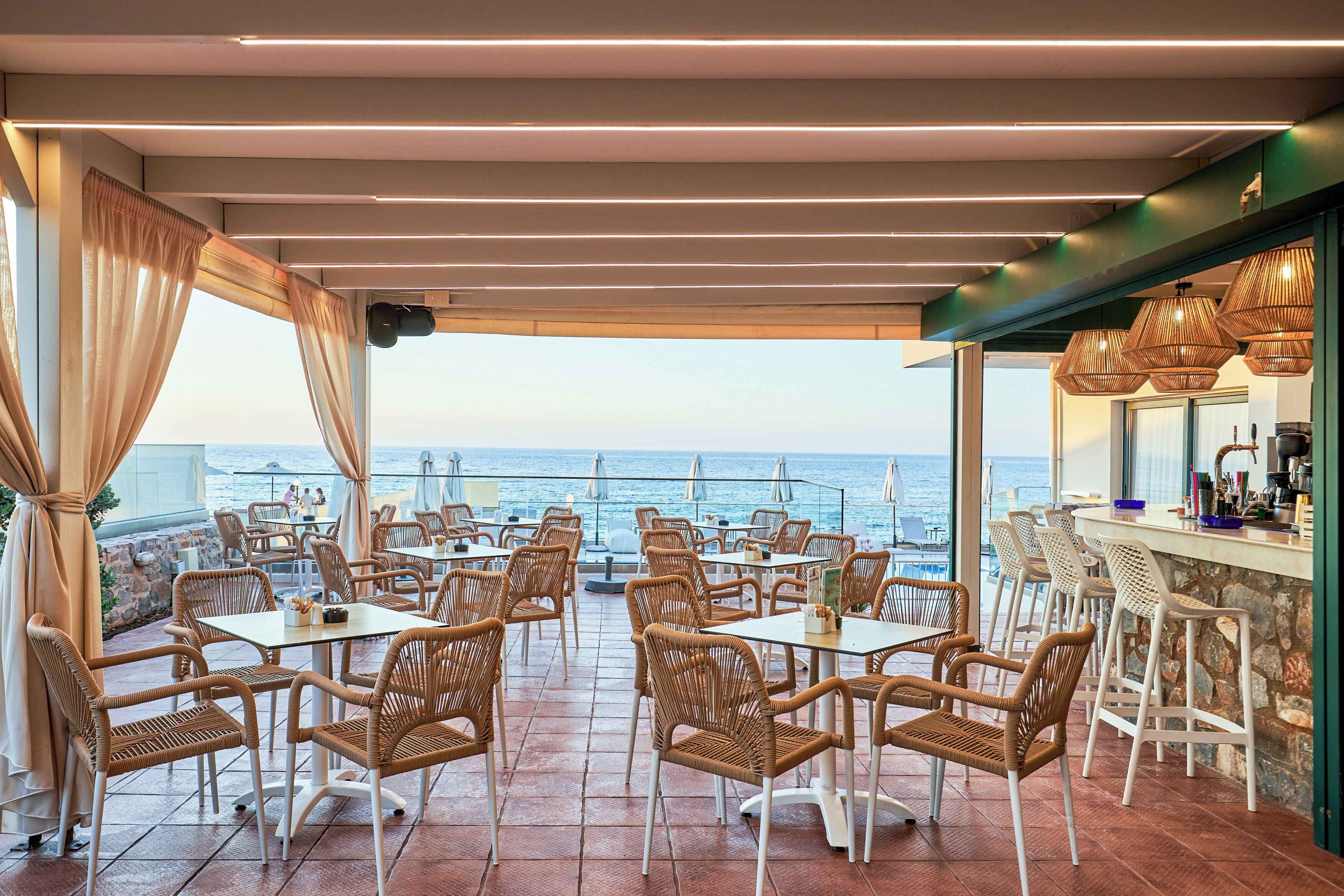 Une terrasse dotée de meubles en osier, d’un bar et offrant une vue sur la mer.