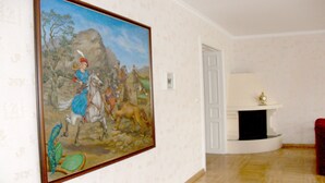 Una habitación con un cuadro grande de una escena histórica, chimenea y una puerta que da a otra estancia.