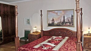 Una cama con dosel con un edredón rojo y blanco estampado, una silla verde, una mesita con una lámpara y un cuadro de un barco en la pared.