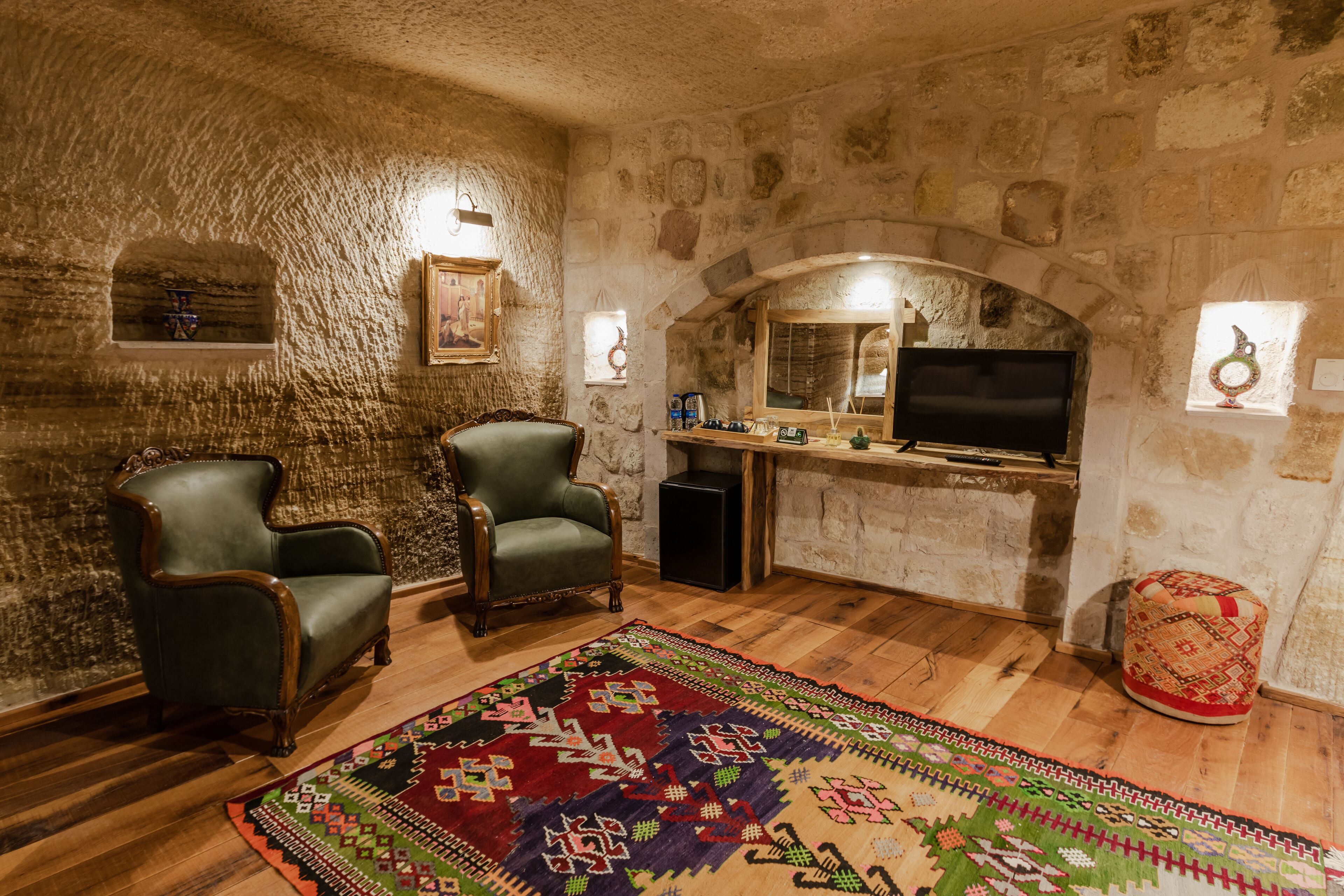 A stone-walled room with two leather armchairs, a television, and a patterned rug.