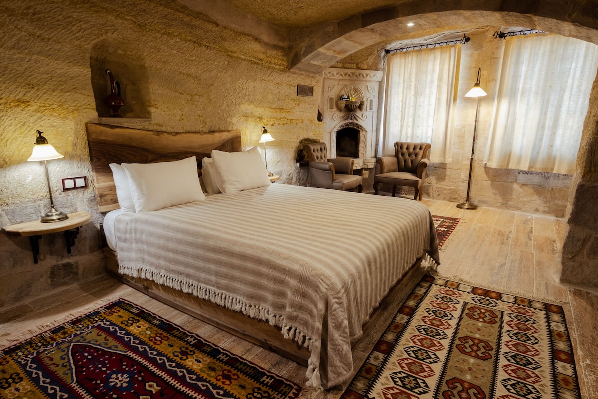 Un dormitorio con una cama grande, dos sillones, una chimenea y una pared de piedra.