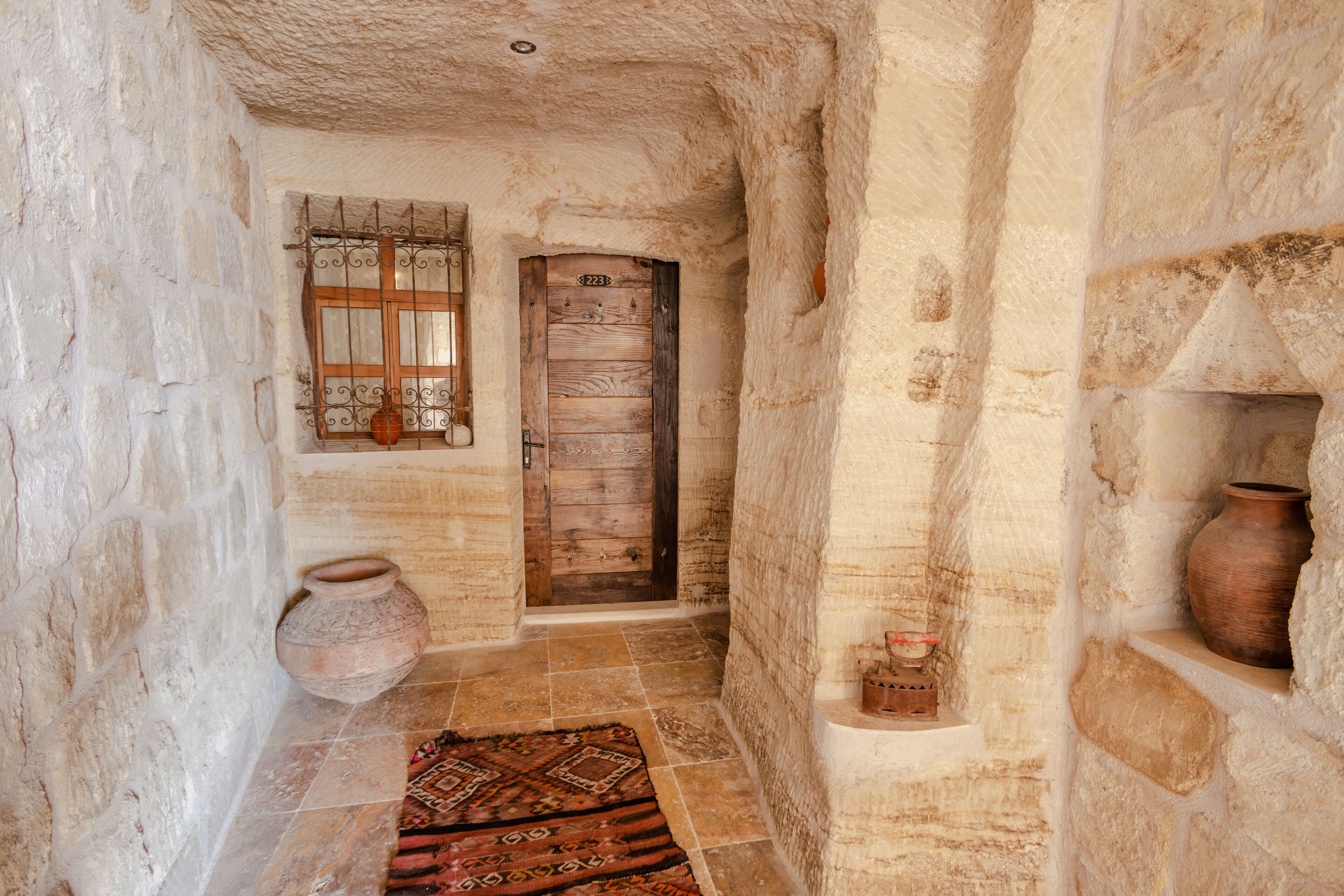Un estrecho pasillo con paredes de piedra, una puerta de madera, una ventana con barrotes y suelo de baldosas.
