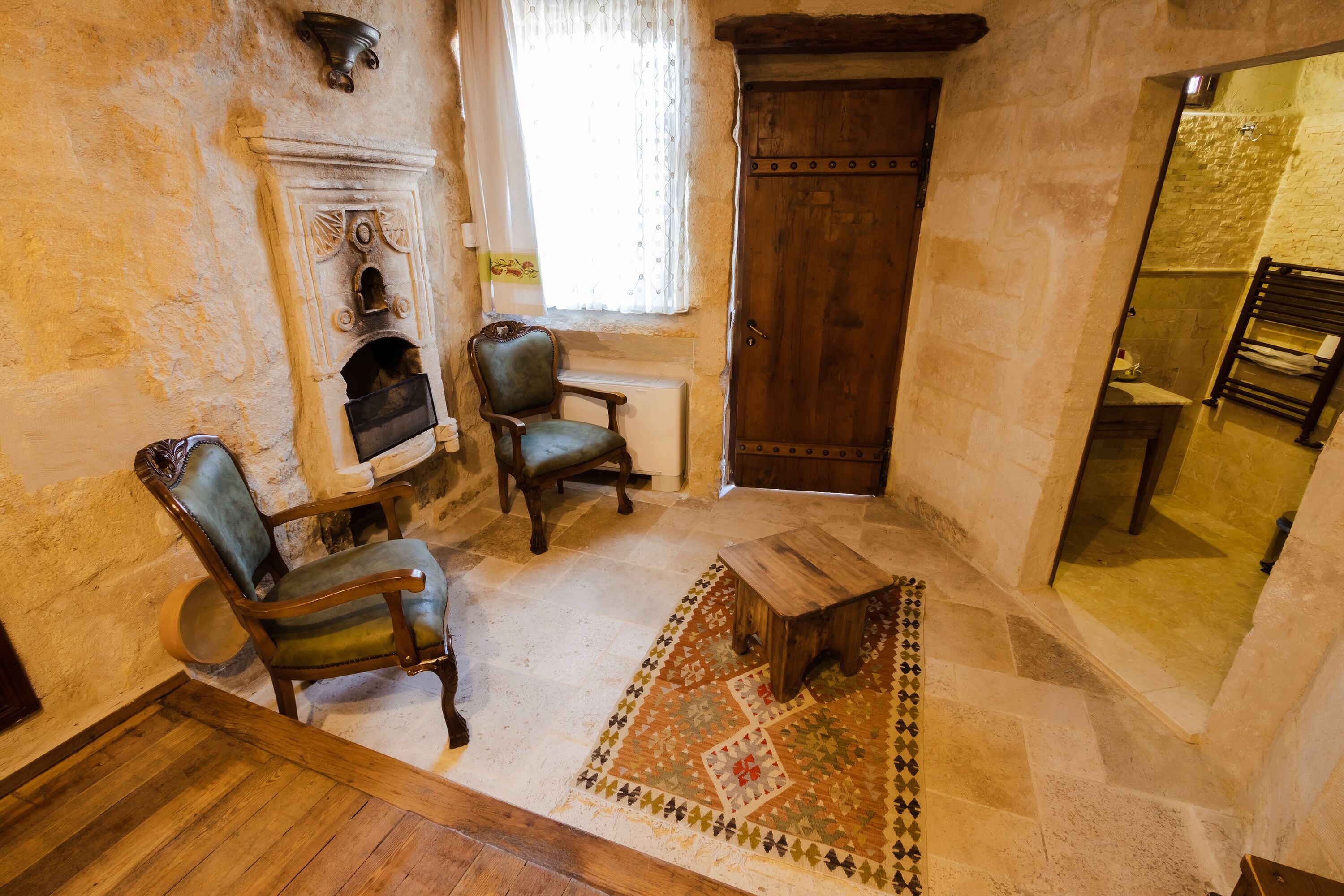 Una habitación tradicional con chimenea, dos sillas de madera, una pequeña mesa de madera y una alfombra estampada.