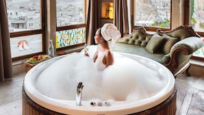 A large wooden hot tub in a room with a view of a cityscape through arched windows. - Sultan Cave Suites (Nevsehir)