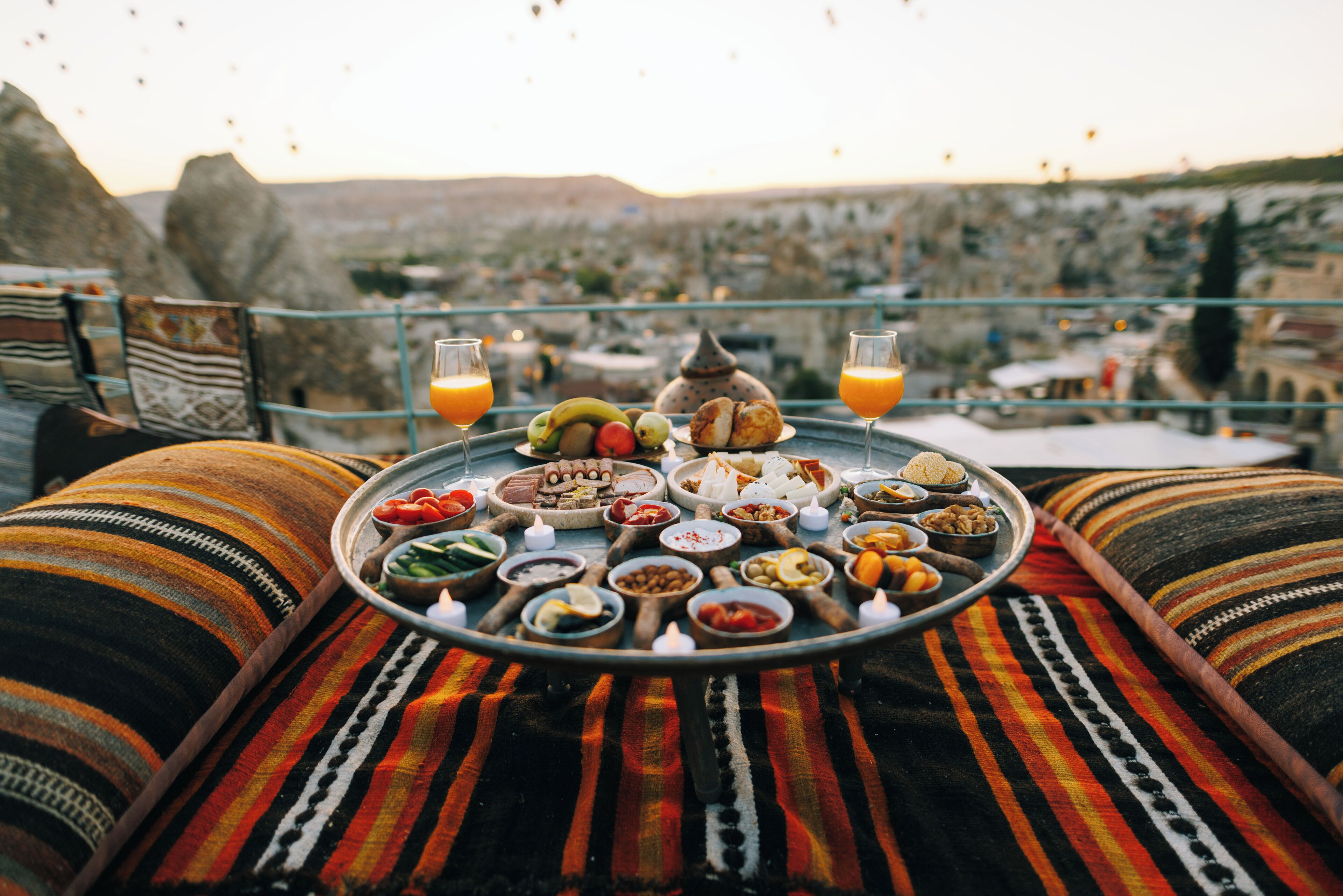 A dining table with a variety of foods and drinks, set on a balcony with a city view.