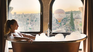 A bathtub in a room with arched windows overlooking a cityscape. - Sultan Cave Suites (Nevsehir)
