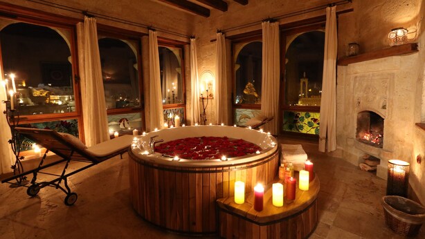 A room with a wooden bathtub filled with rose petals, candles, and a bench. - Sultan Cave Suites (Nevsehir)