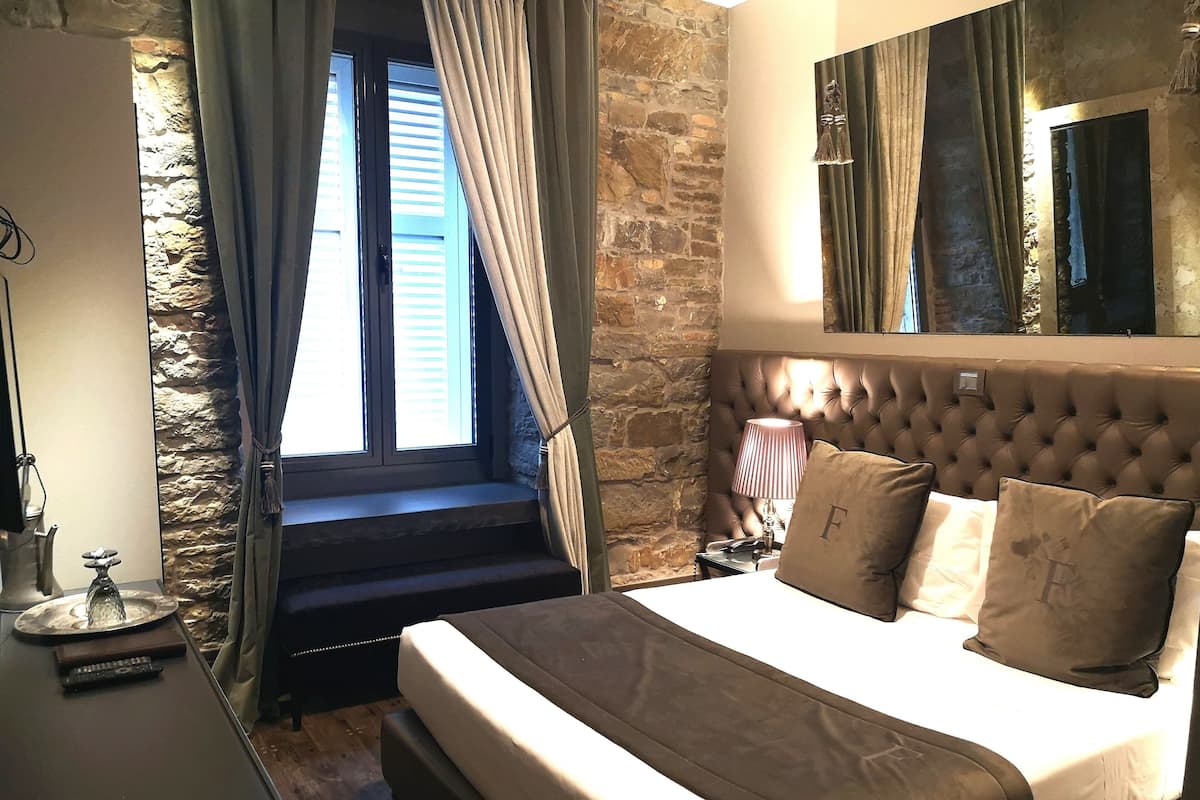 Un dormitorio con una cama grande, pared de piedra y una ventana con cortinas.