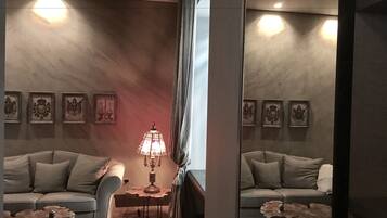 A room with a sofa, a table with a lamp, and framed pictures on the wall.