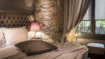 Un dormitorio con pared de piedra, cabecera capitonada, mesita de noche con lámpara y ventana con vistas.