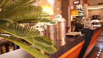 Una zona de bar con mostrador pulido, una planta decorativa y diversos artículos de bar.