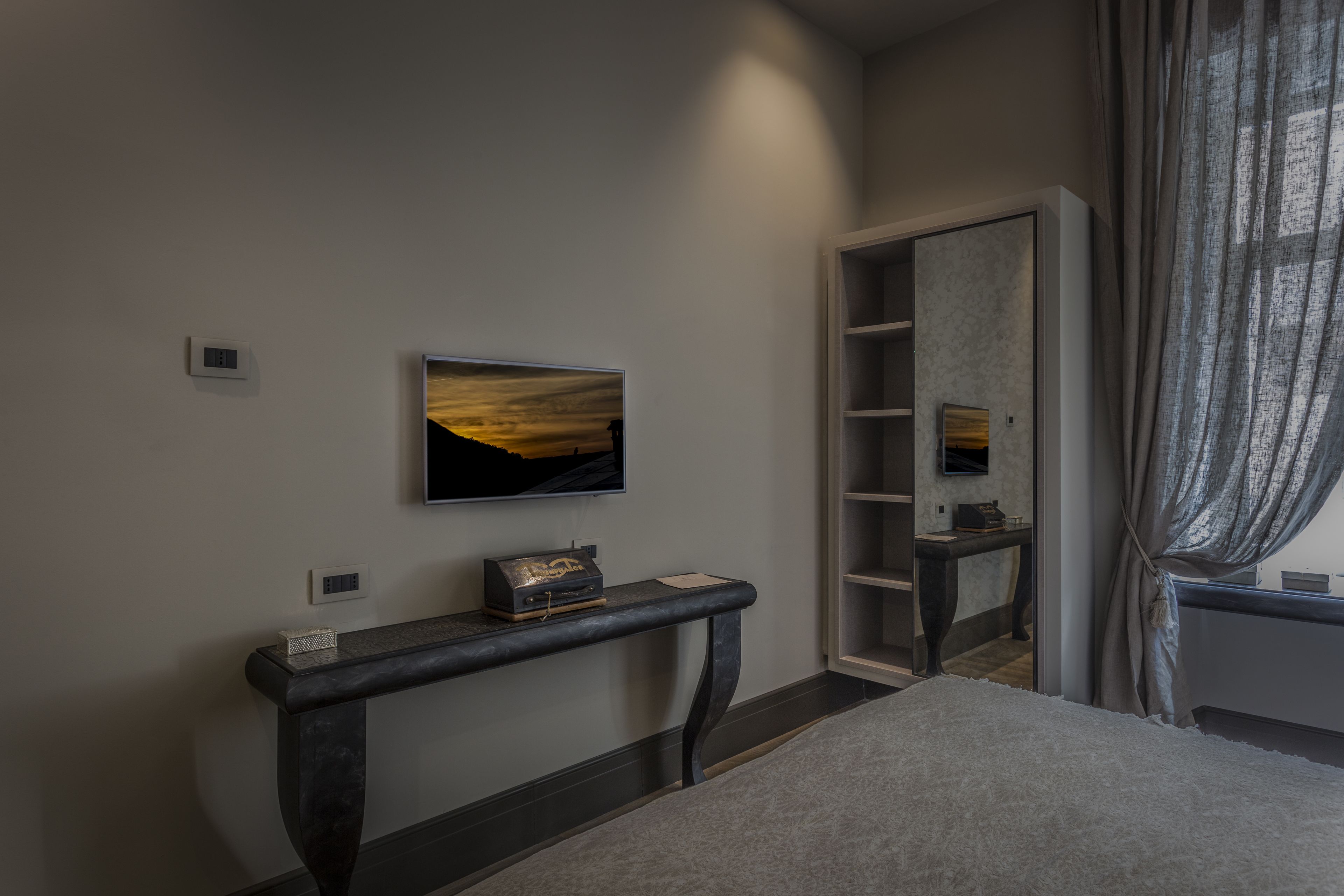 A bedroom with a bed, a console table with a small decorative item, a painting, and a built-in shelving unit.