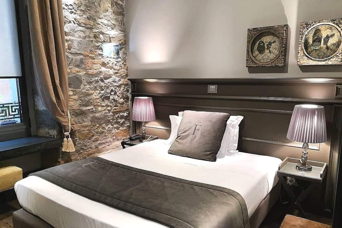 Una habitación de hotel con una cama grande, dos lámparas de noche, una pared de piedra y obras de arte en la pared.